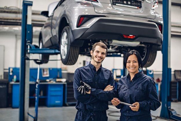 Two smiling technicians under a car on a lift